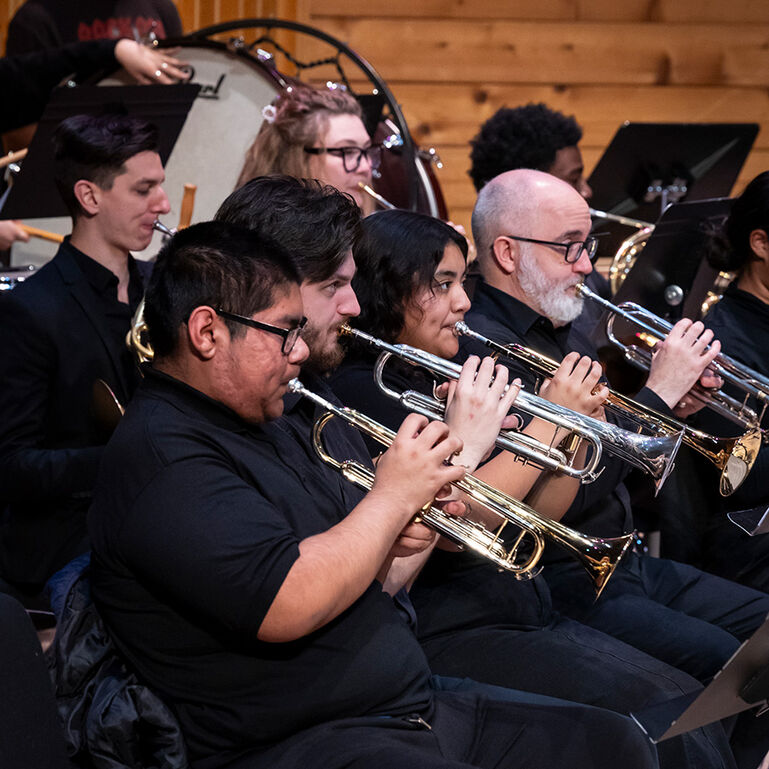 Students playing trumpet on stage in a concert band