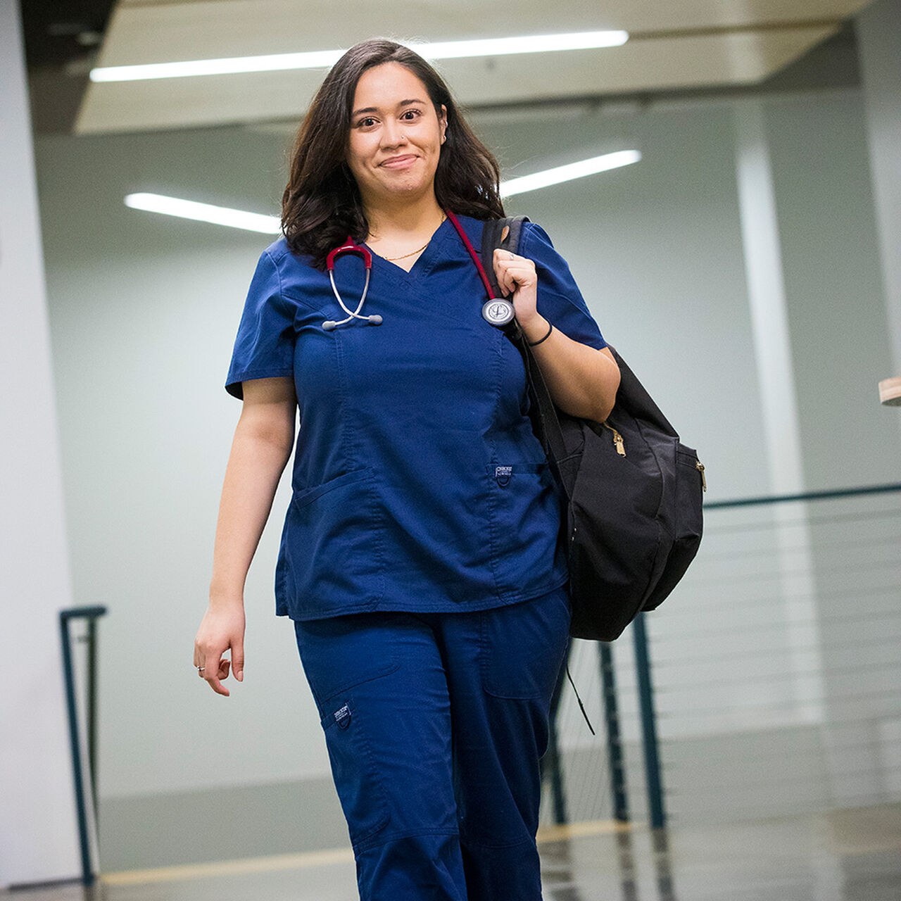 Nursing student in scrubs walking and holding a backpack over one shoulder image number 0