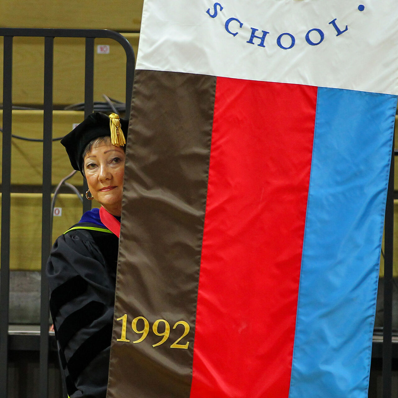 Student in cap and gown standing with Bloustein school flag image number 0