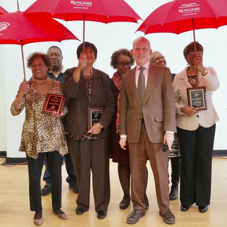 A group of people standing and smiling at the camera holding up red umbrellas