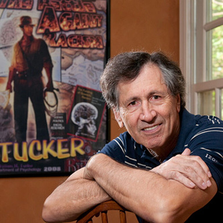 Professor Tucker sitting in a chair in front of a poster that reads Tucker