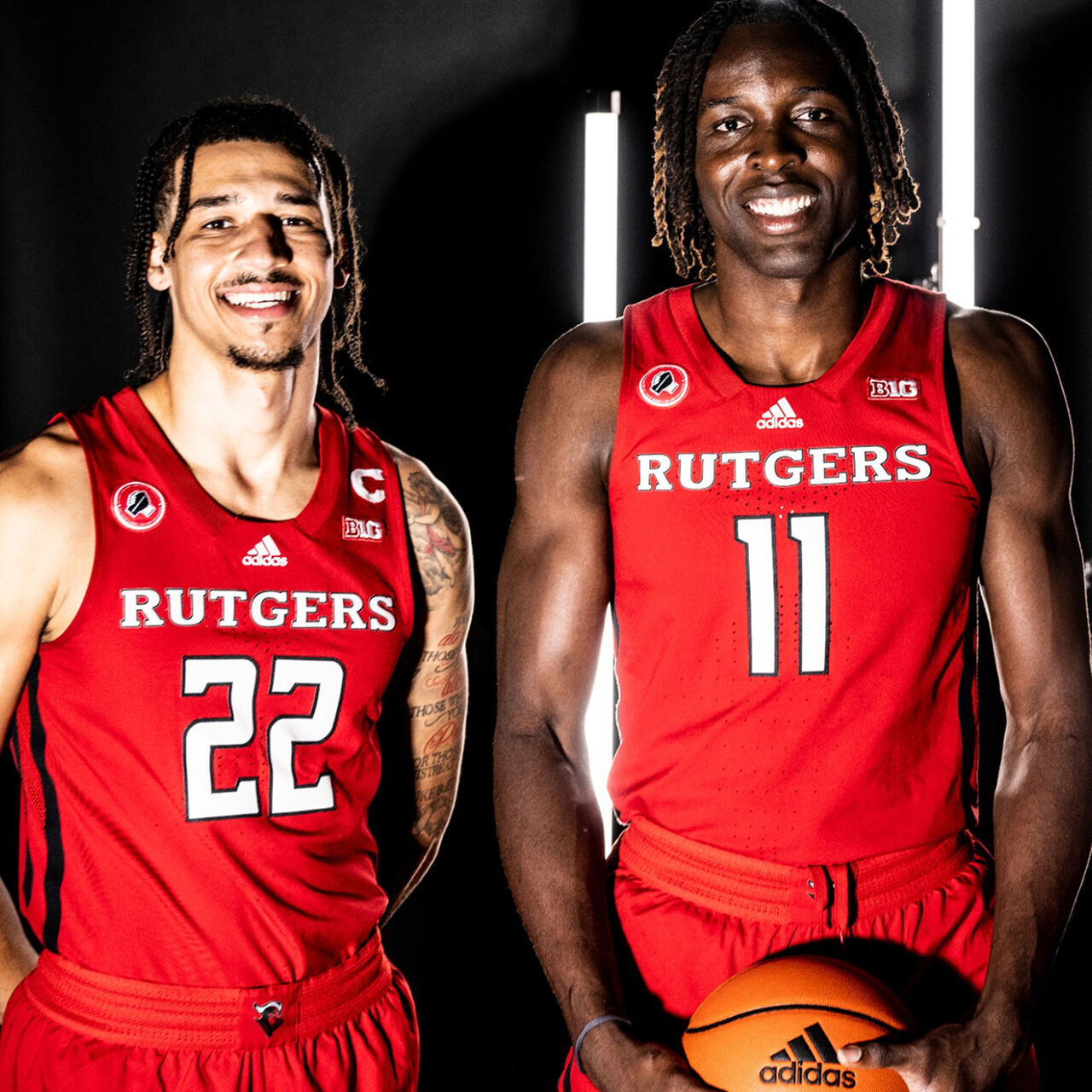 Two Scarlet Knight men's basketball players in their jersey's smiling with bright lights behind them image number 0