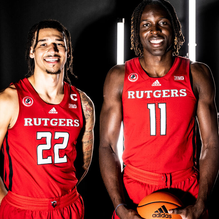 Two Scarlet Knight men's basketball players in their jersey's smiling with bright lights behind them