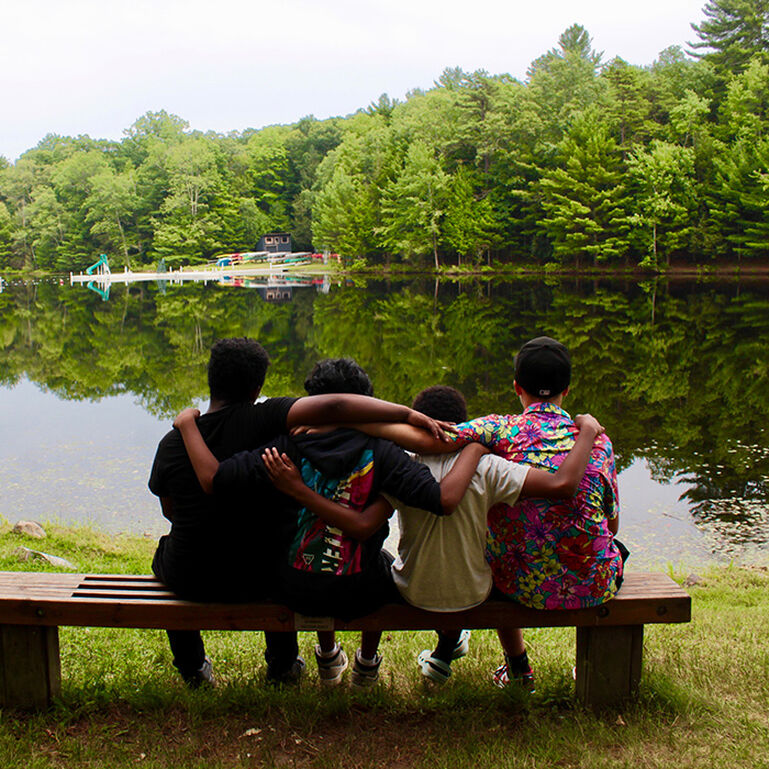 Group of campers sitting on a bench together near a lake