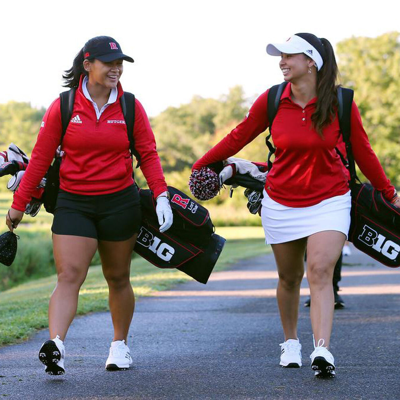 Two Rutgers Women's Golf players walking down a path and carrying their clubs while talking image number 0