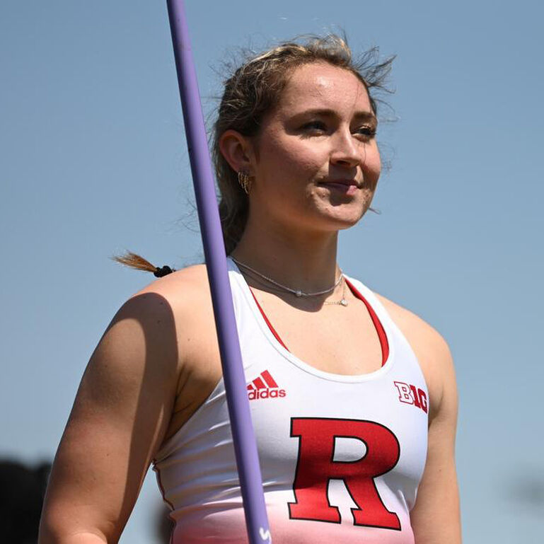 Rutgers pole vaulter standing and smiling while holding a pole