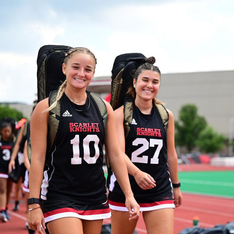 Two Rutgers Field Hockey players smiling at the camera on the outdoor track