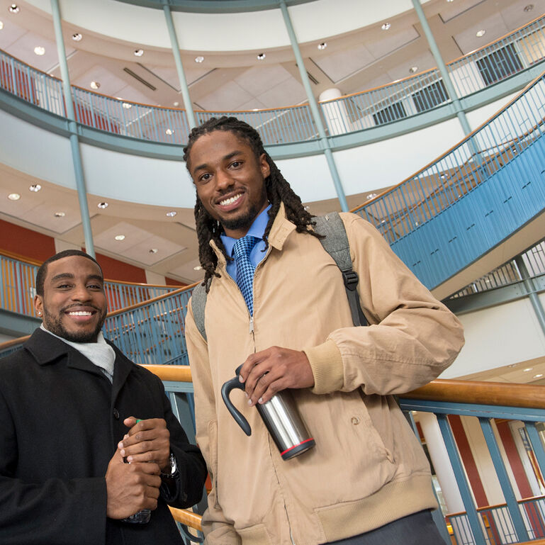 2 students smiling and standing on stairs inside the Center for Law & Justice building at Rutgers-Newark
