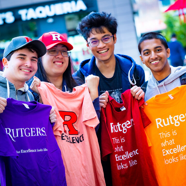 Students smiling and holding up Rutgers Excellence t-shirts in The Yard on the College Avenue campus