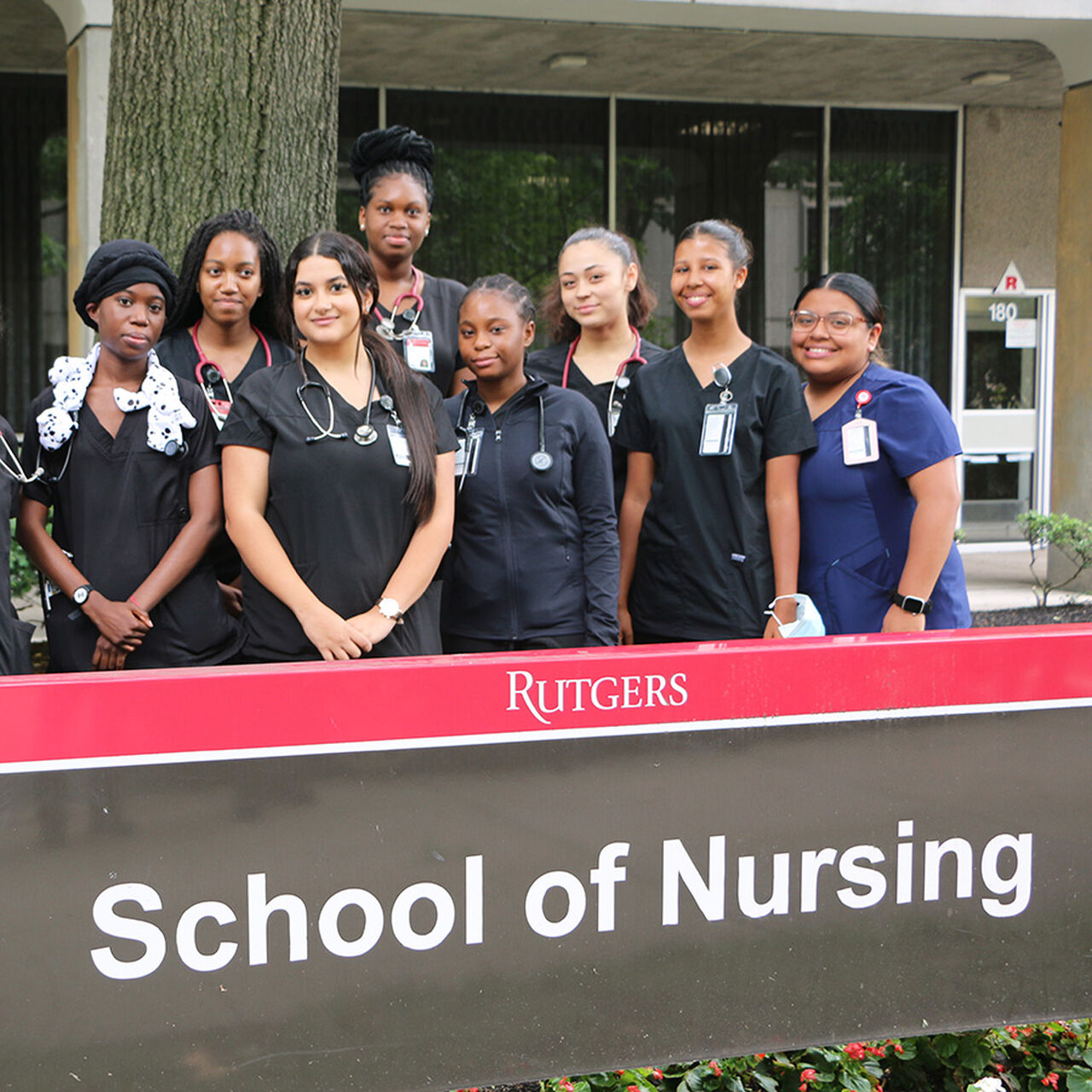 A group of nursing students in scrubs standing behind the Rutgers School of Nursing sign image number 0