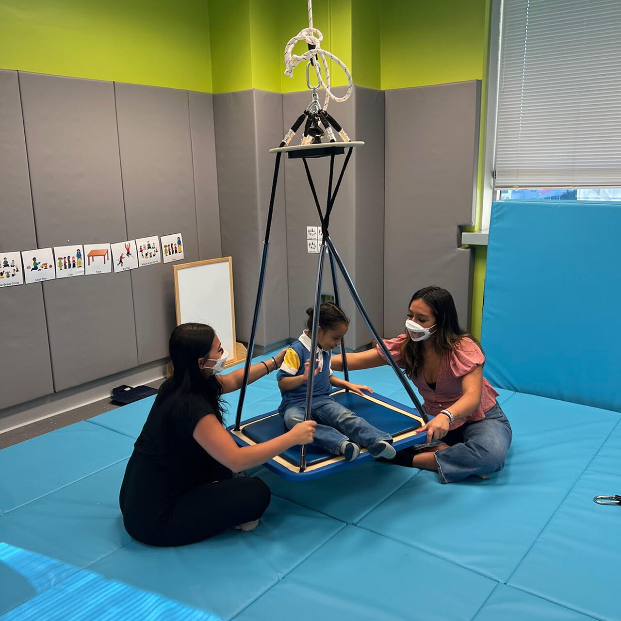 Two practitioners working with a child on an indoor swing image number 2